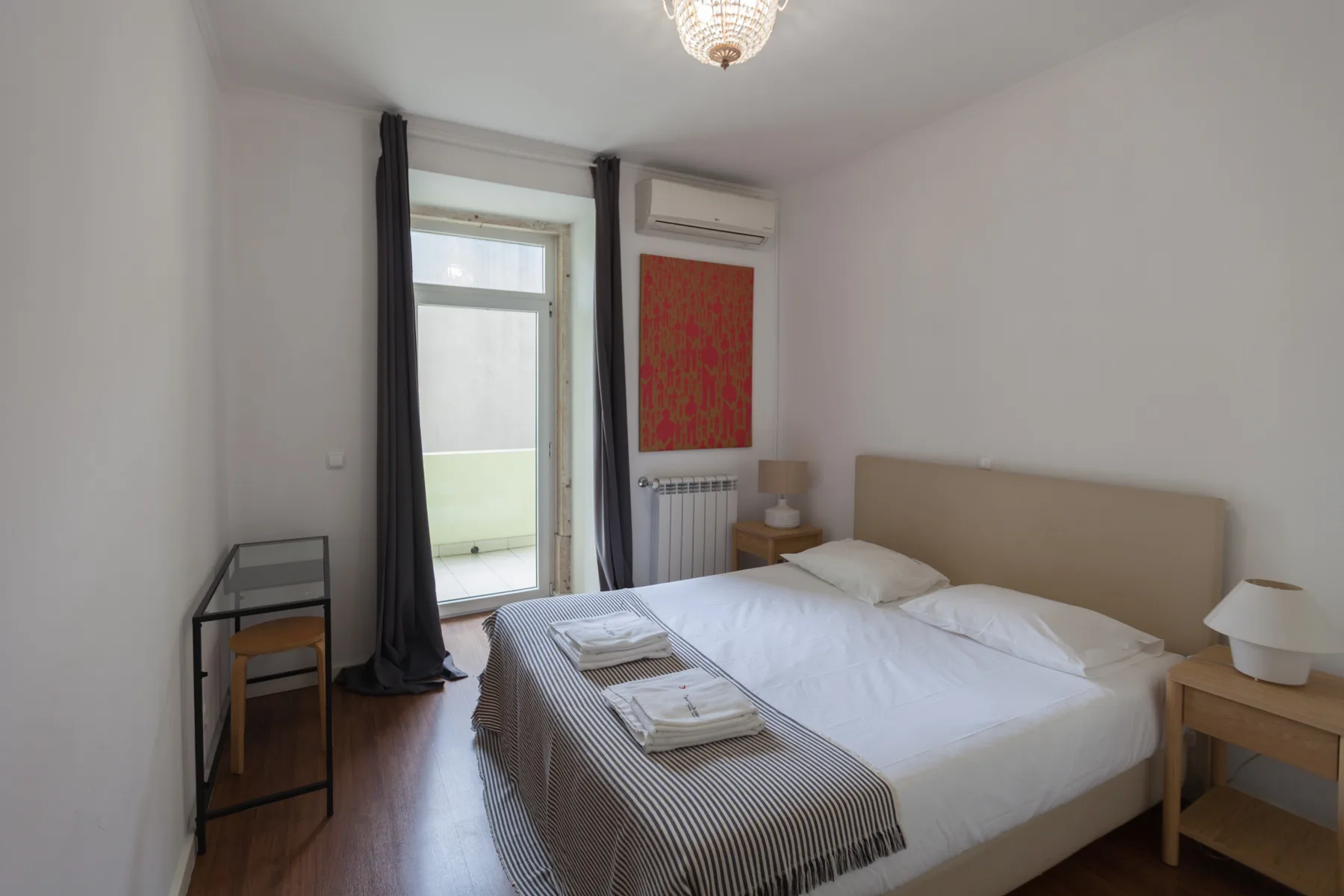 A bright bedroom with a double bed and a glass door to a balcony.