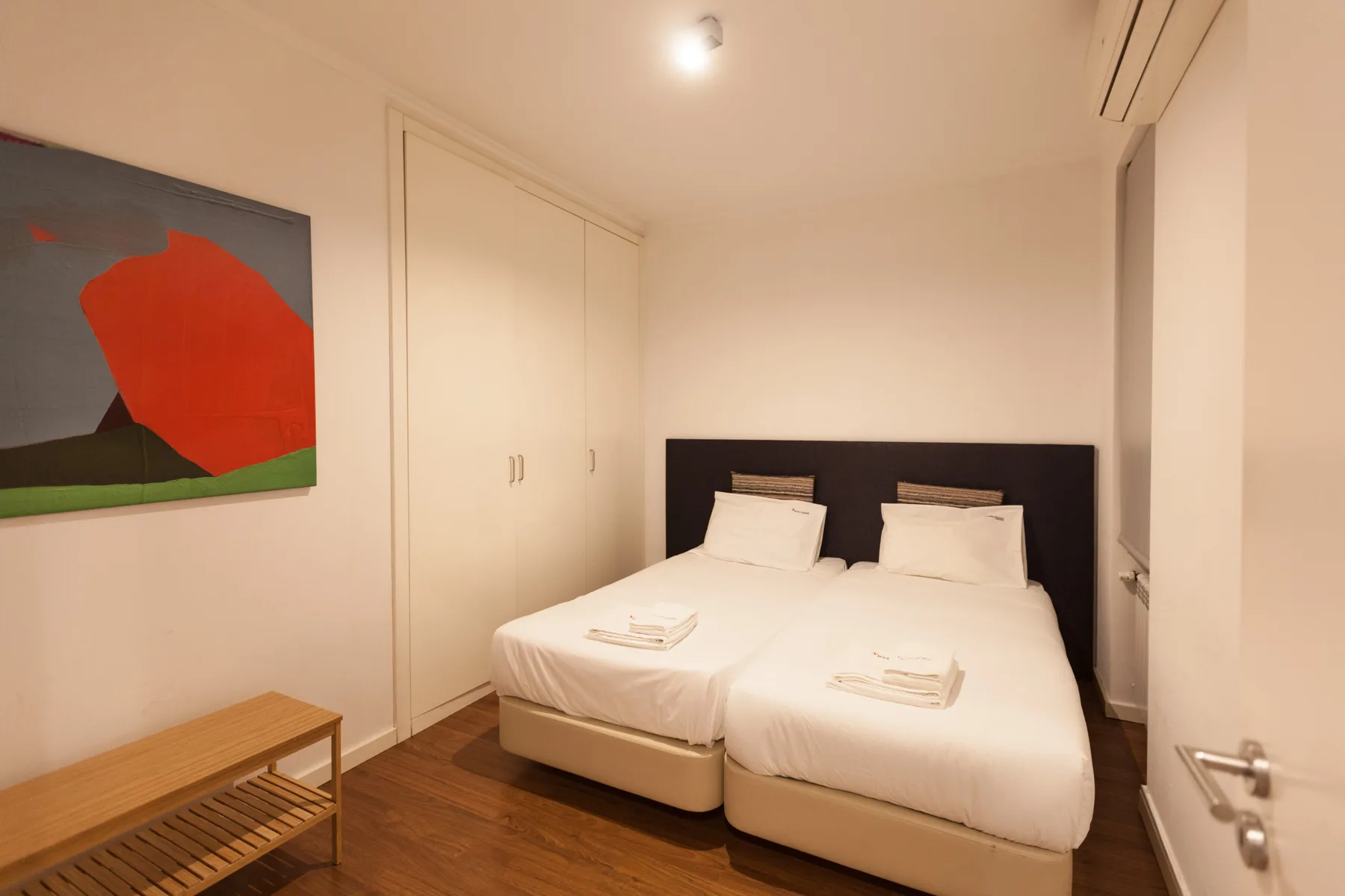A bedroom with two beds, a wardrobe, and colorful wall art.