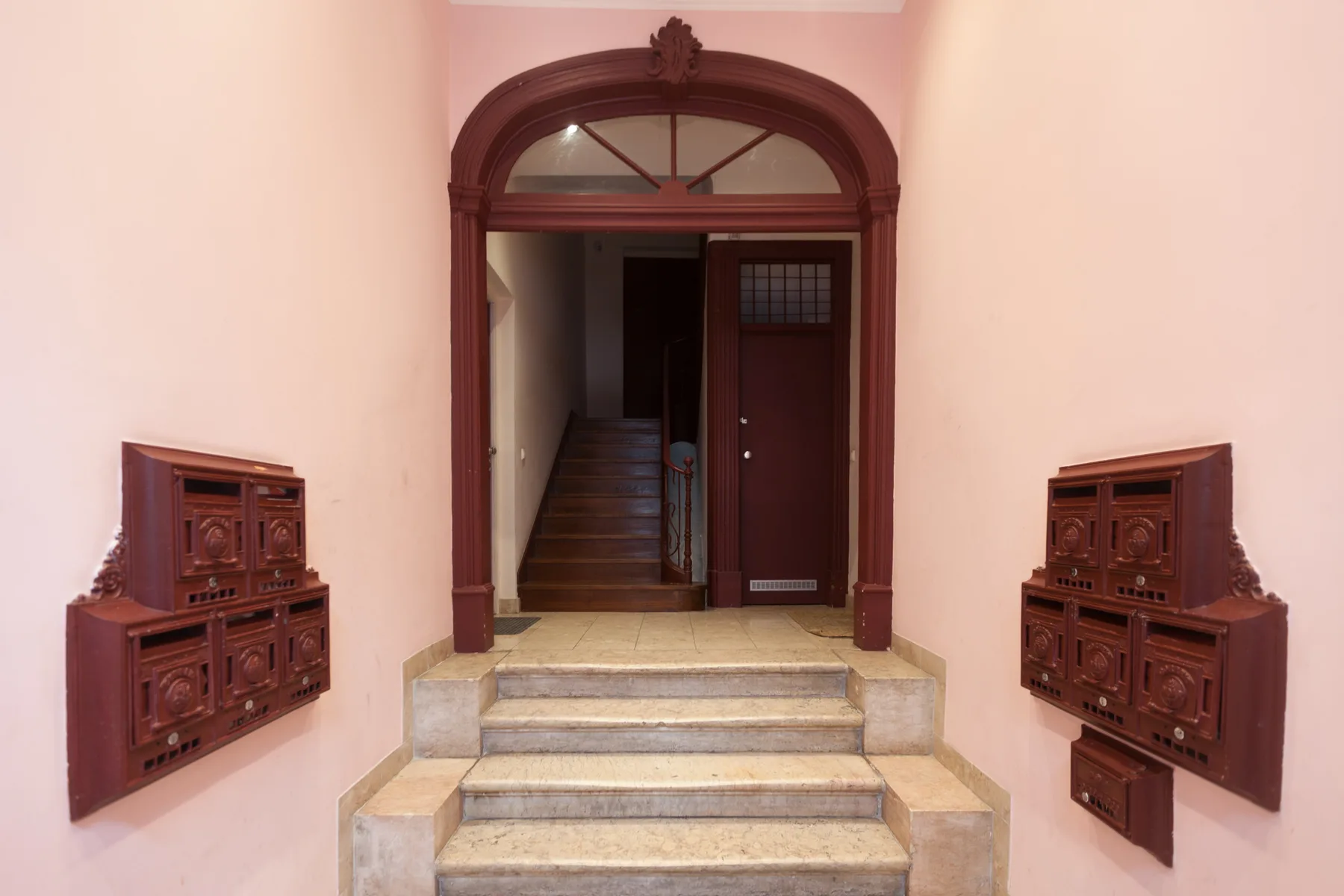 A pink entryway with a dark wooden arched doorway and stone steps.