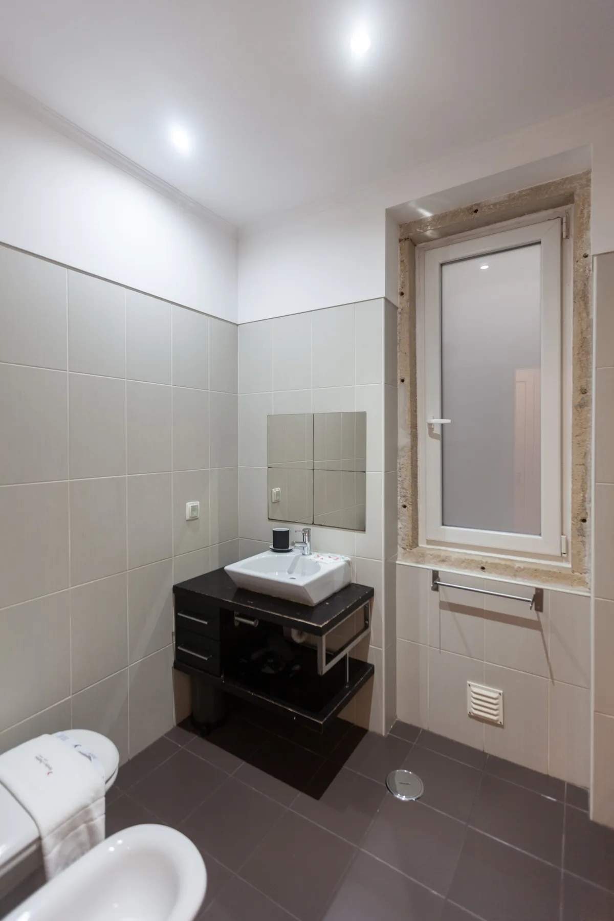 A tiled bathroom with a sink beneath a window.