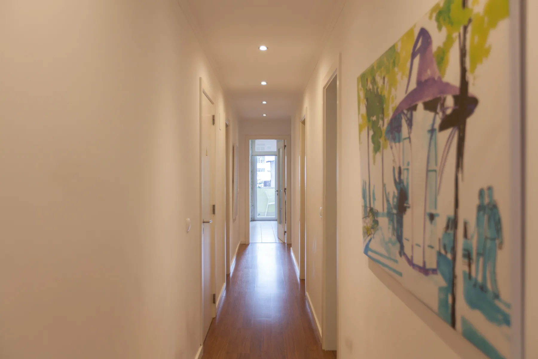A bright hallway with wooden flooring and colorful artwork on the wall.