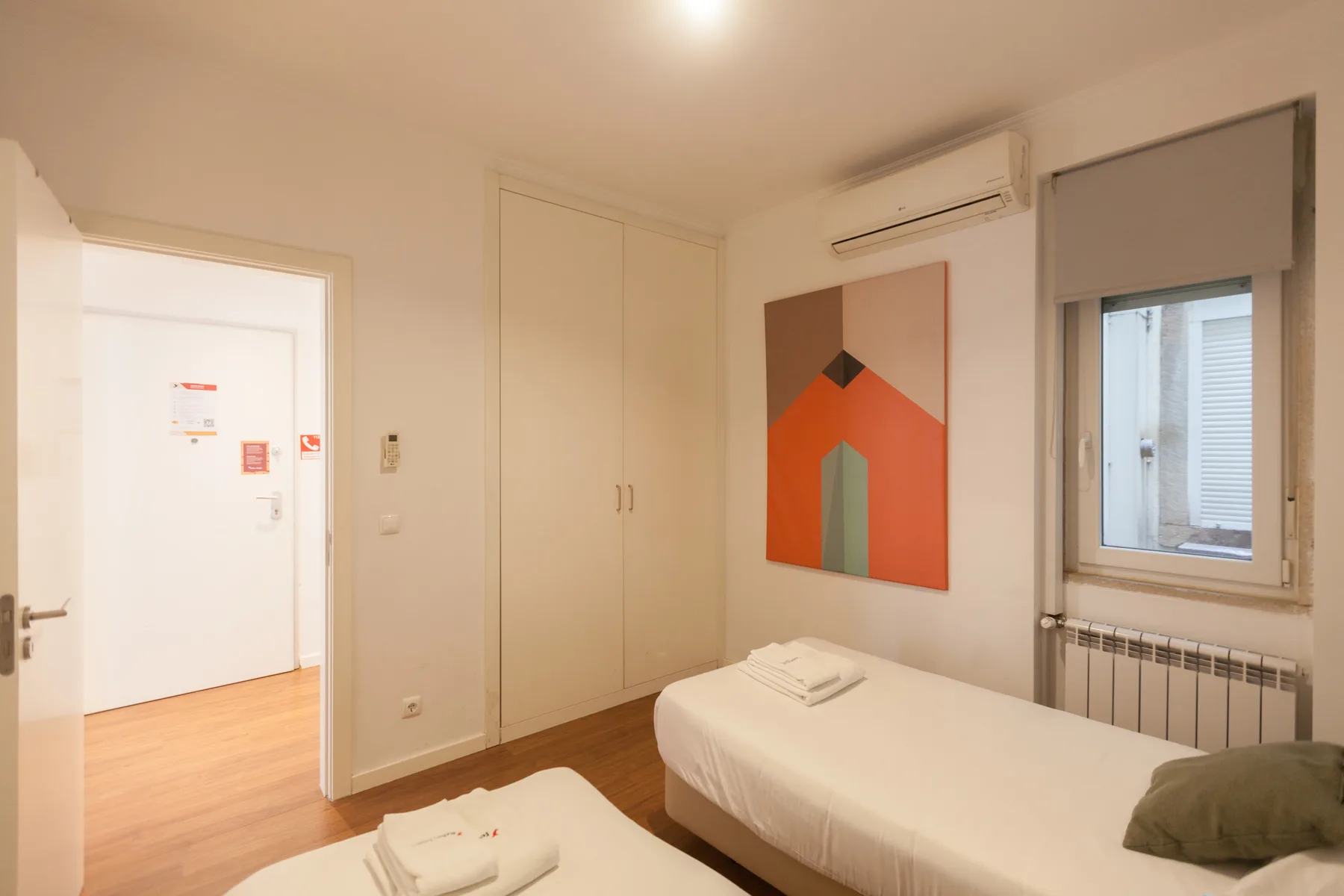 A bedroom with two beds, a wardrobe, and a window.