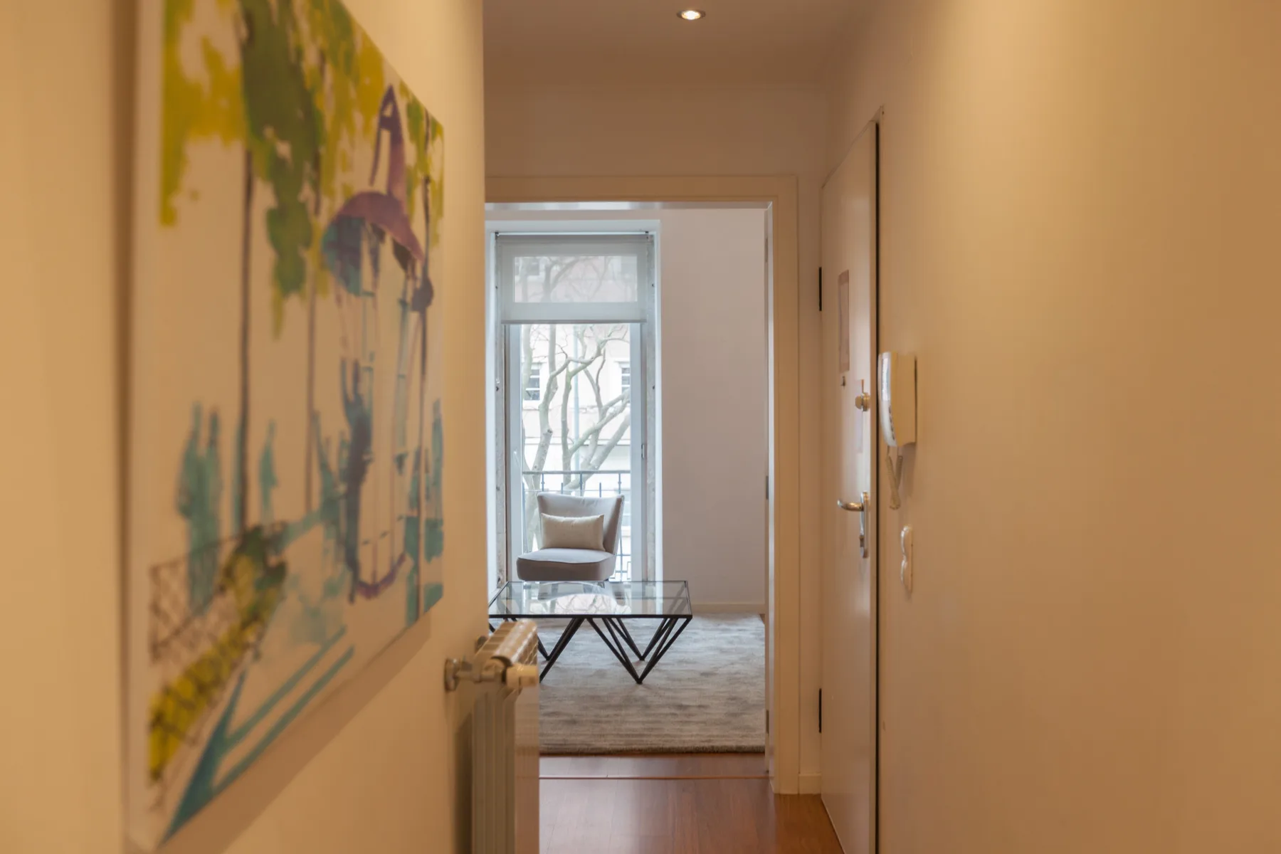 A hallway leads to a living area with seating and a large window.