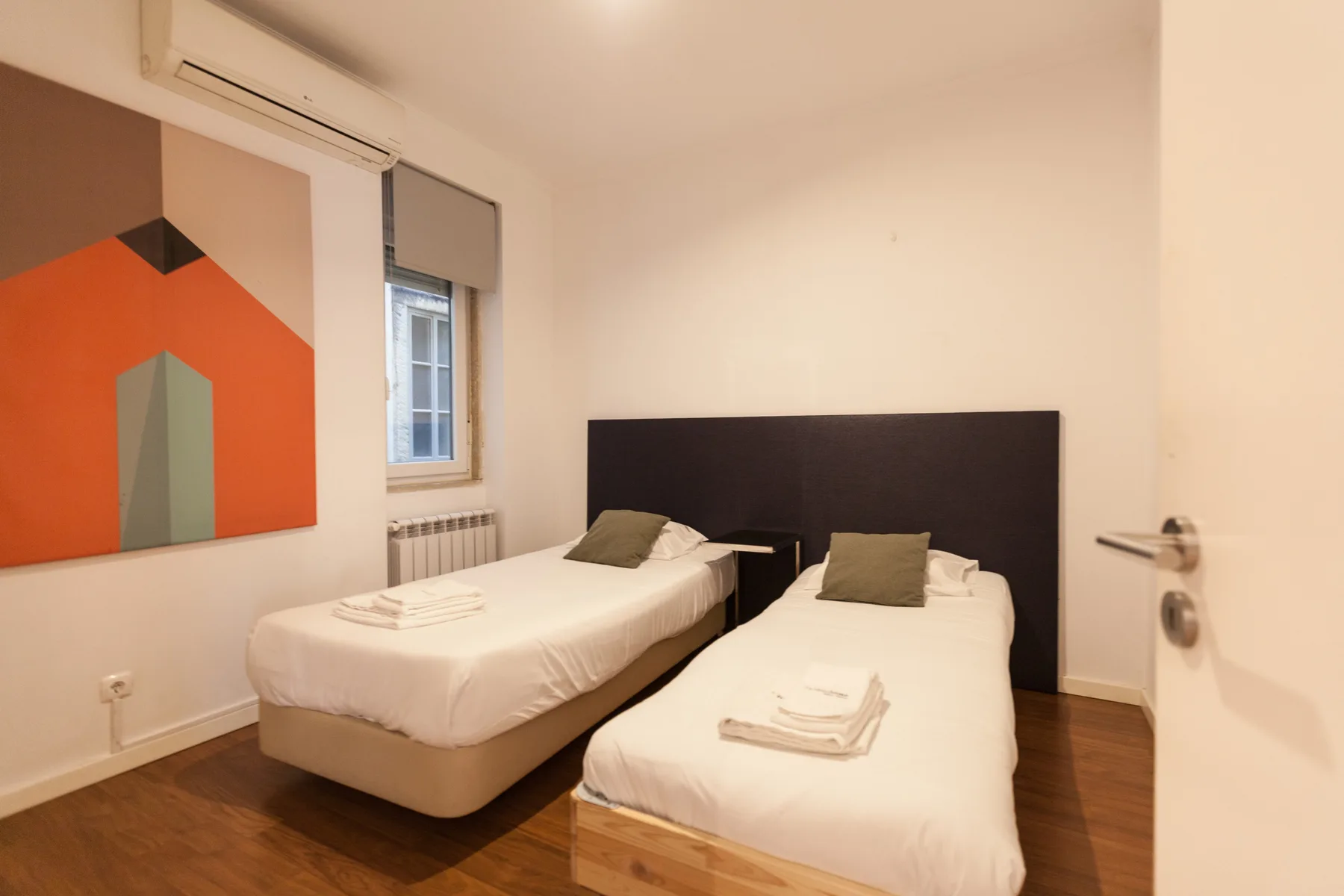 A bedroom with two beds, a window, and geometric wall art.