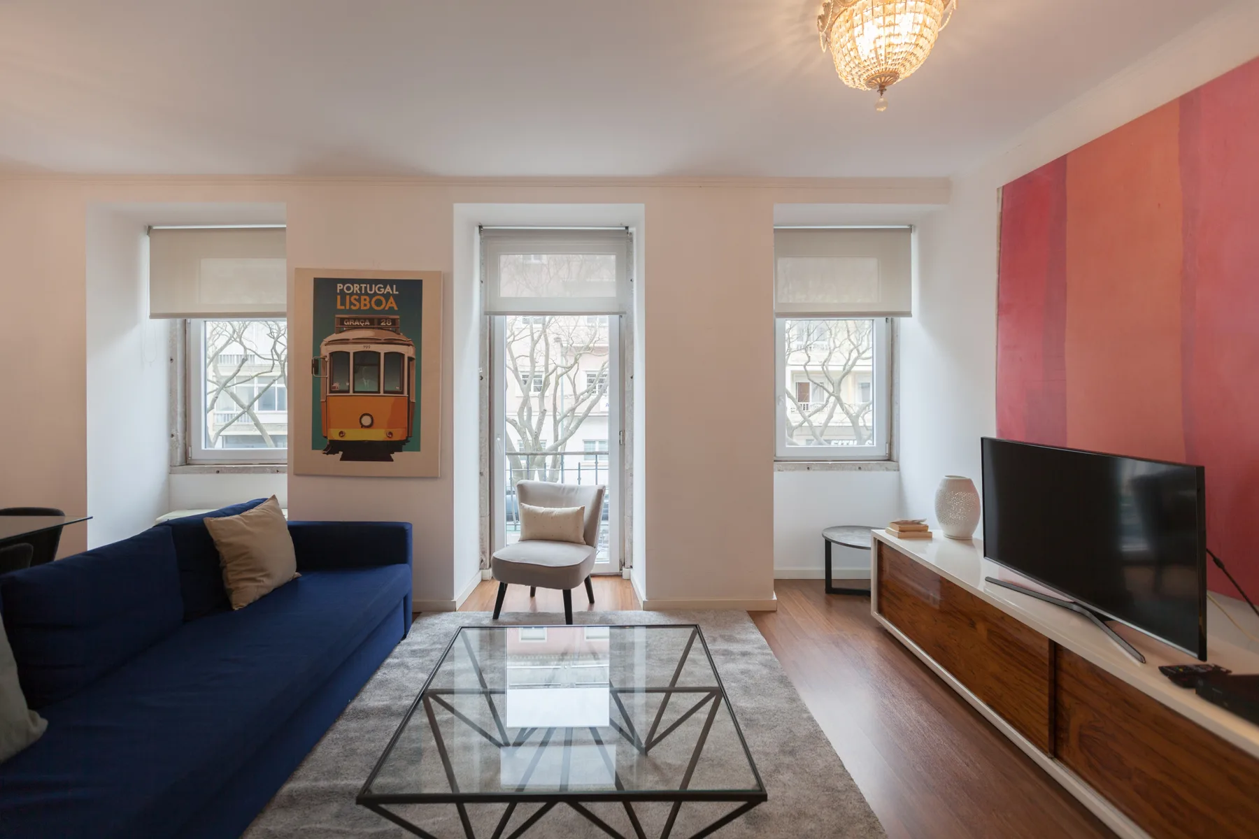 Living room with blue seating, a glass coffee table, and a television.