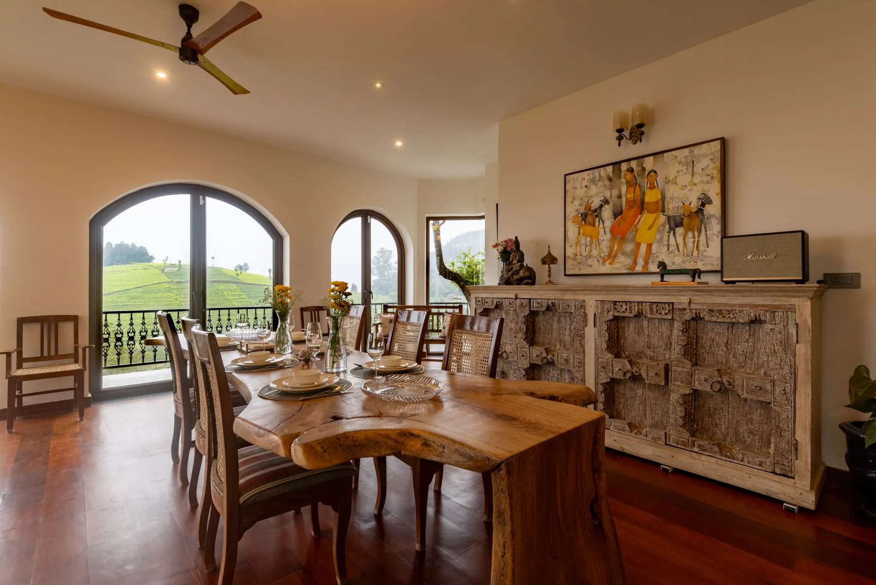 A dining room with a long wooden table and arched windows overlooking green fields.