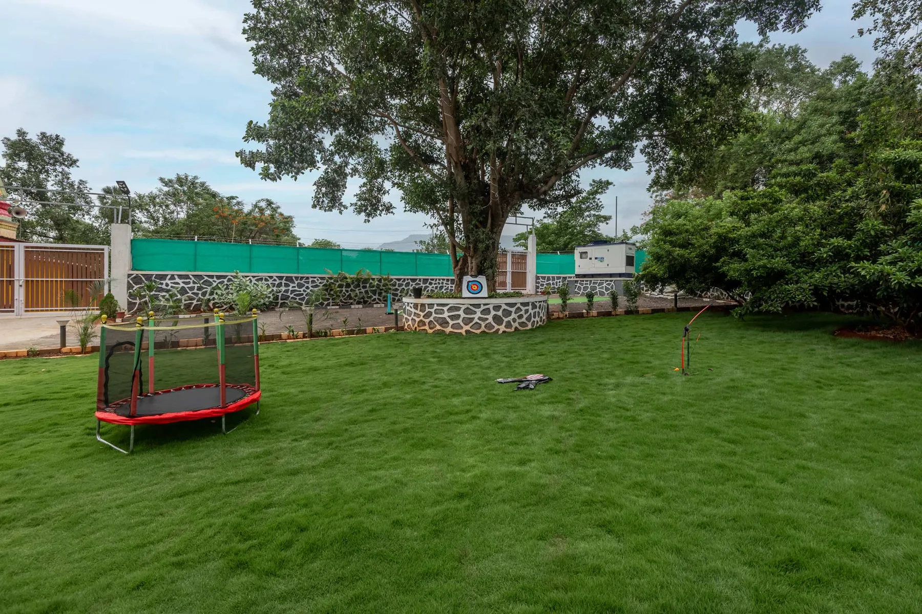 Zona recreativa al aire libre con césped, pequeños juegos y un árbol grande.
