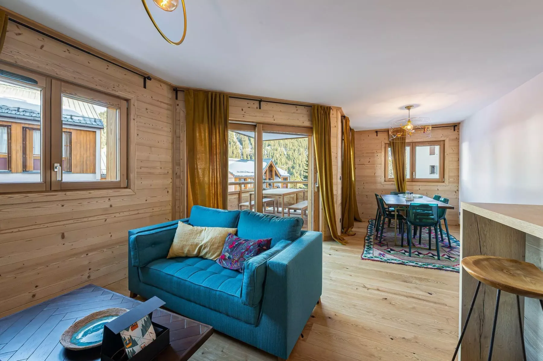 Sala de estar y comedor con paredes de madera, asientos azules y una mesa junto a las ventanas.