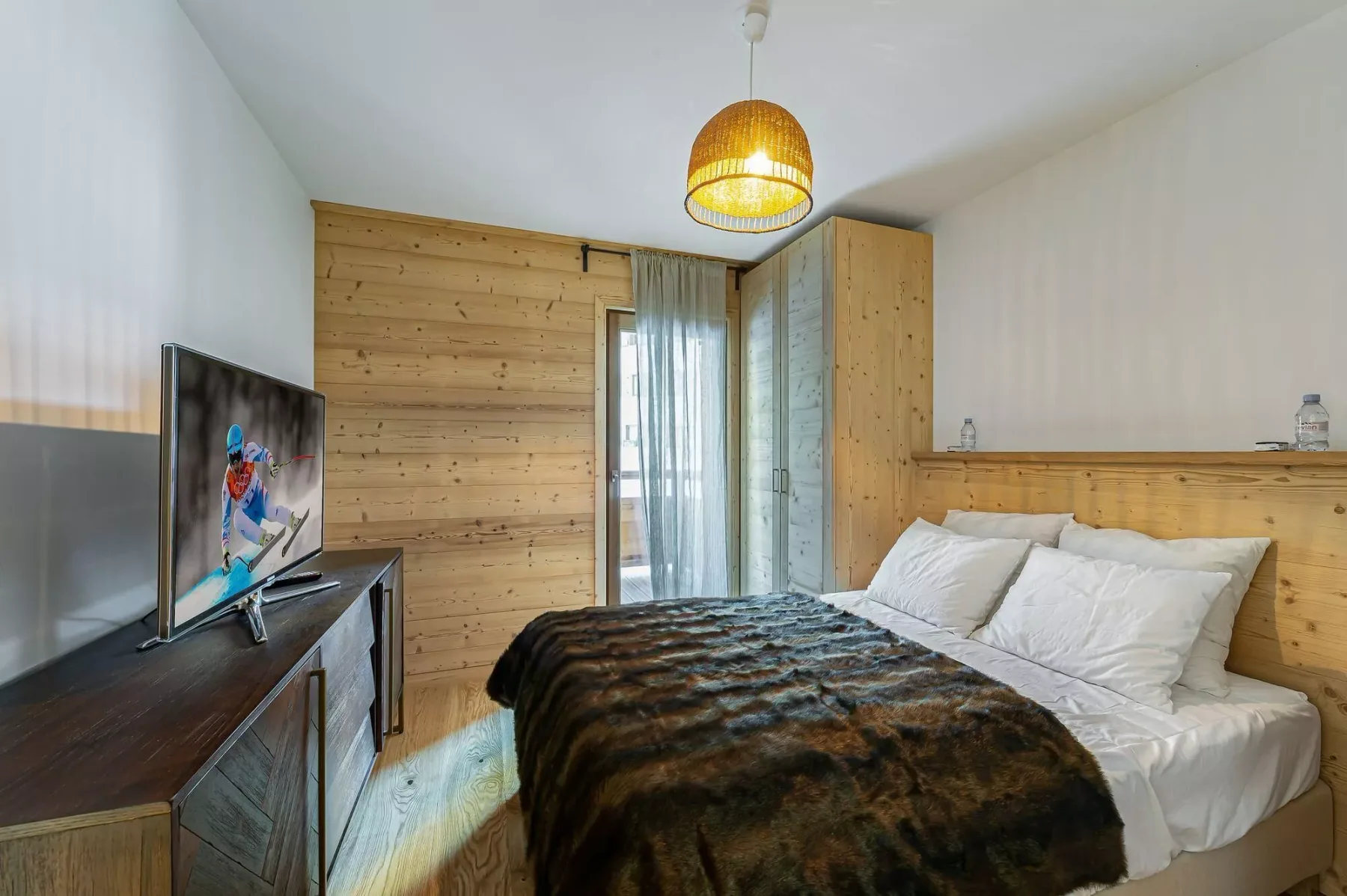 A bedroom with a bed, white bedding, and a television on a wooden cabinet.
