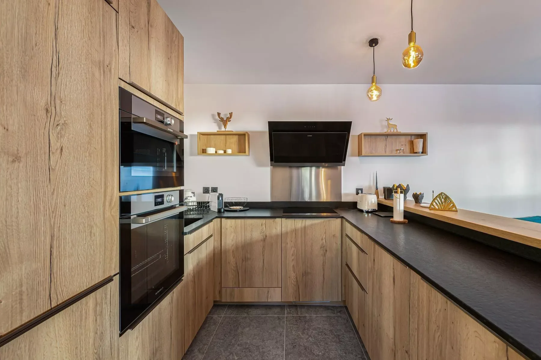 Una cocina moderna con gabinetes de madera, encimeras oscuras y electrodomésticos integrados.
