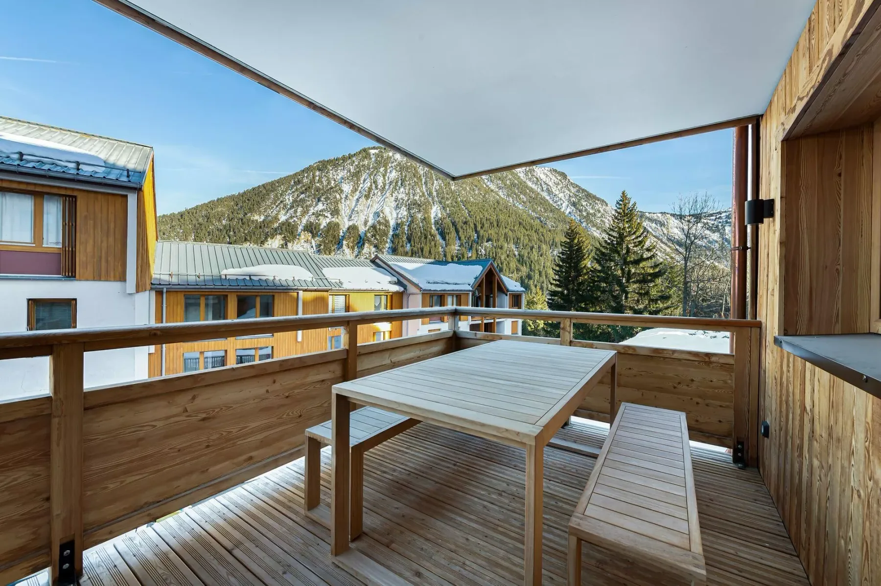 Una terraza de madera con mesa y banco da a un paisaje montañoso.