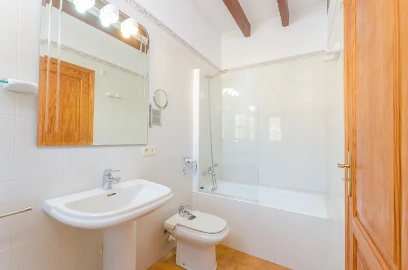 A bright bathroom with a sink, toilet, and glass shower screen.