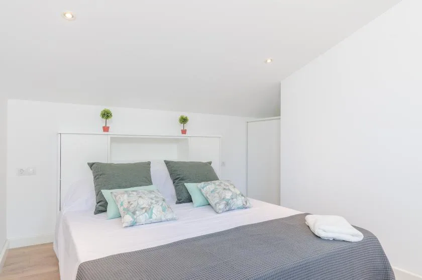 A bright bedroom with a neatly made bed and green accent pillows.