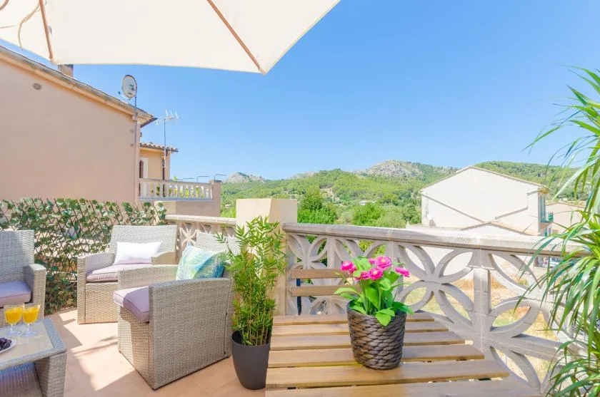 Una terraza soleada con asientos acolchados, plantas en macetas y una barandilla decorativa.