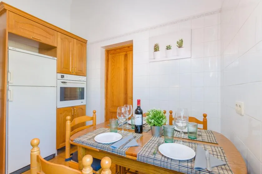 A small dining area with a set table beside a refrigerator and wooden cabinets.