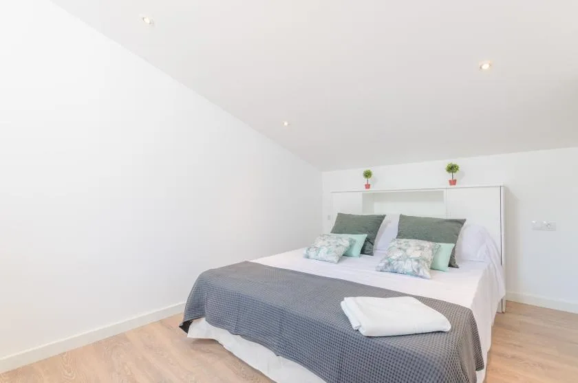 A bright bedroom with a bed dressed in gray bedding and small plants on the headboard.