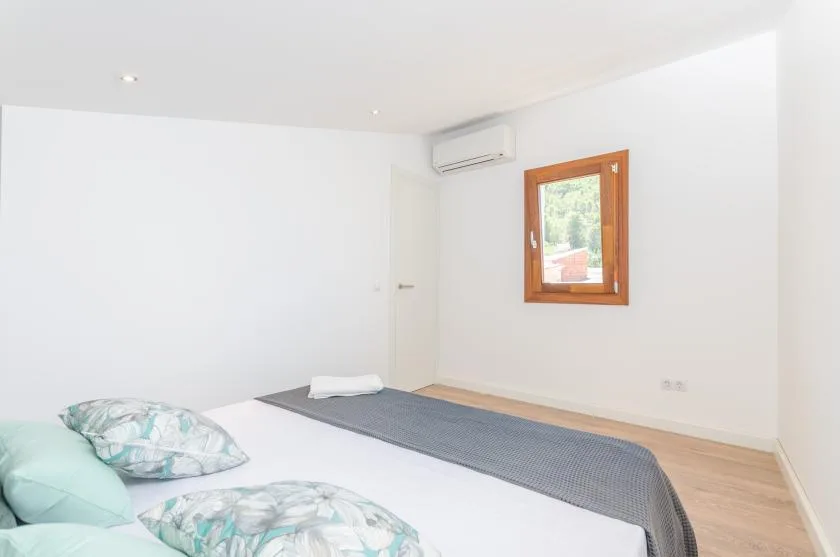 A bright bedroom with a bed, a small window, and a wall-mounted air conditioner.