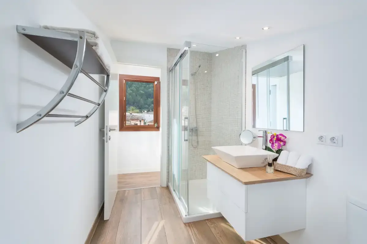 A bright bathroom with a glass shower, vessel sink, and wall-mounted towel rack.