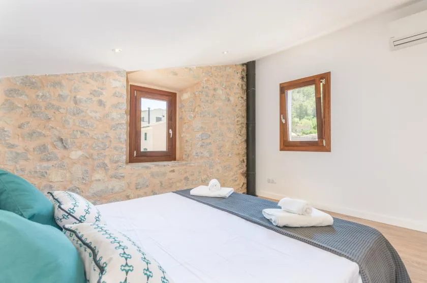 A bedroom with a bed, stone-patterned walls, and two windows.