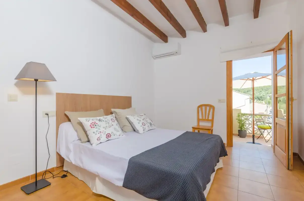 A bedroom with a neatly made bed and an open doorway to a balcony.