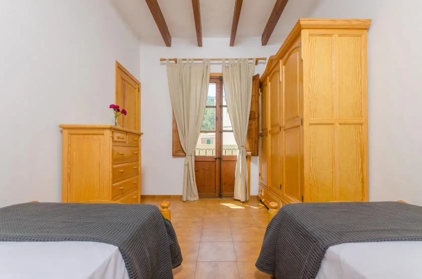 A bedroom with two beds, wooden wardrobes, and a curtained window.