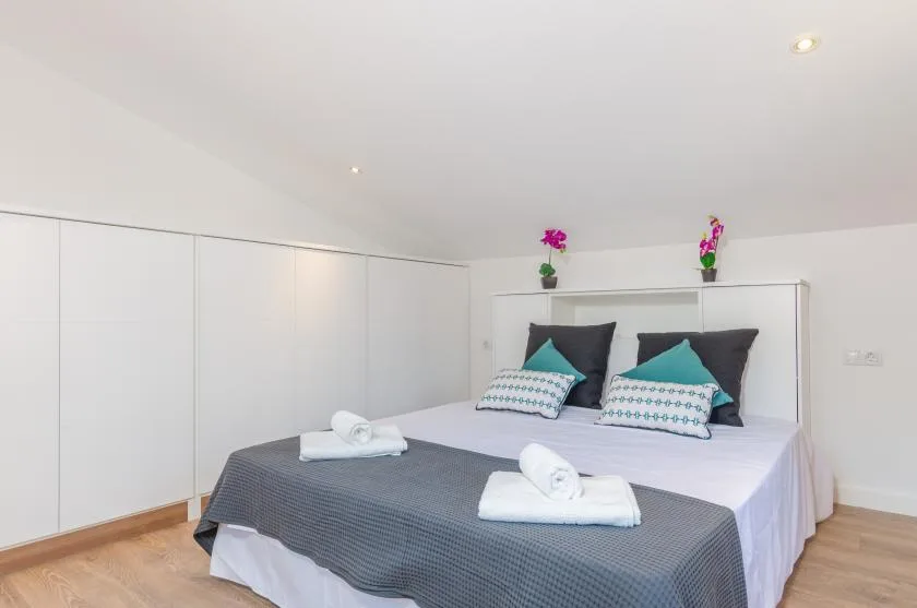 A bright bedroom with a neatly made bed and built-in white cabinets.