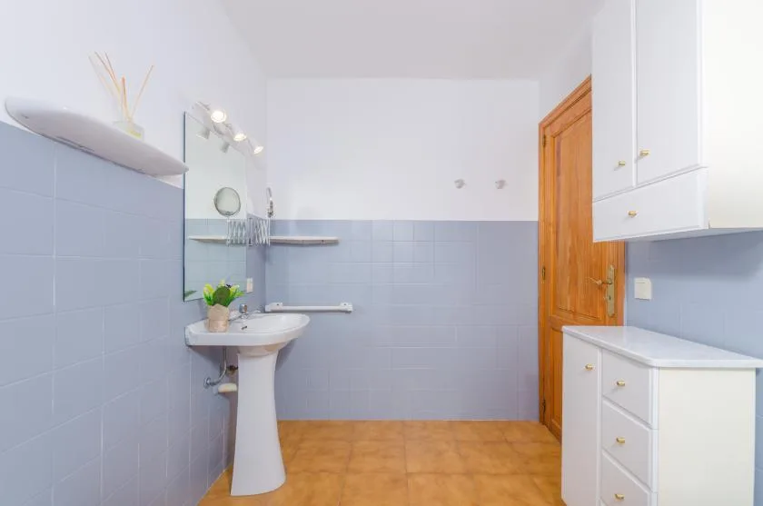A bathroom with a pedestal sink, mirror, and white storage cabinets.