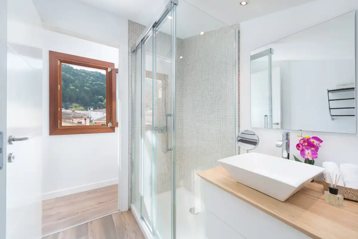A bright bathroom with a glass shower and a vessel sink on a wood counter.