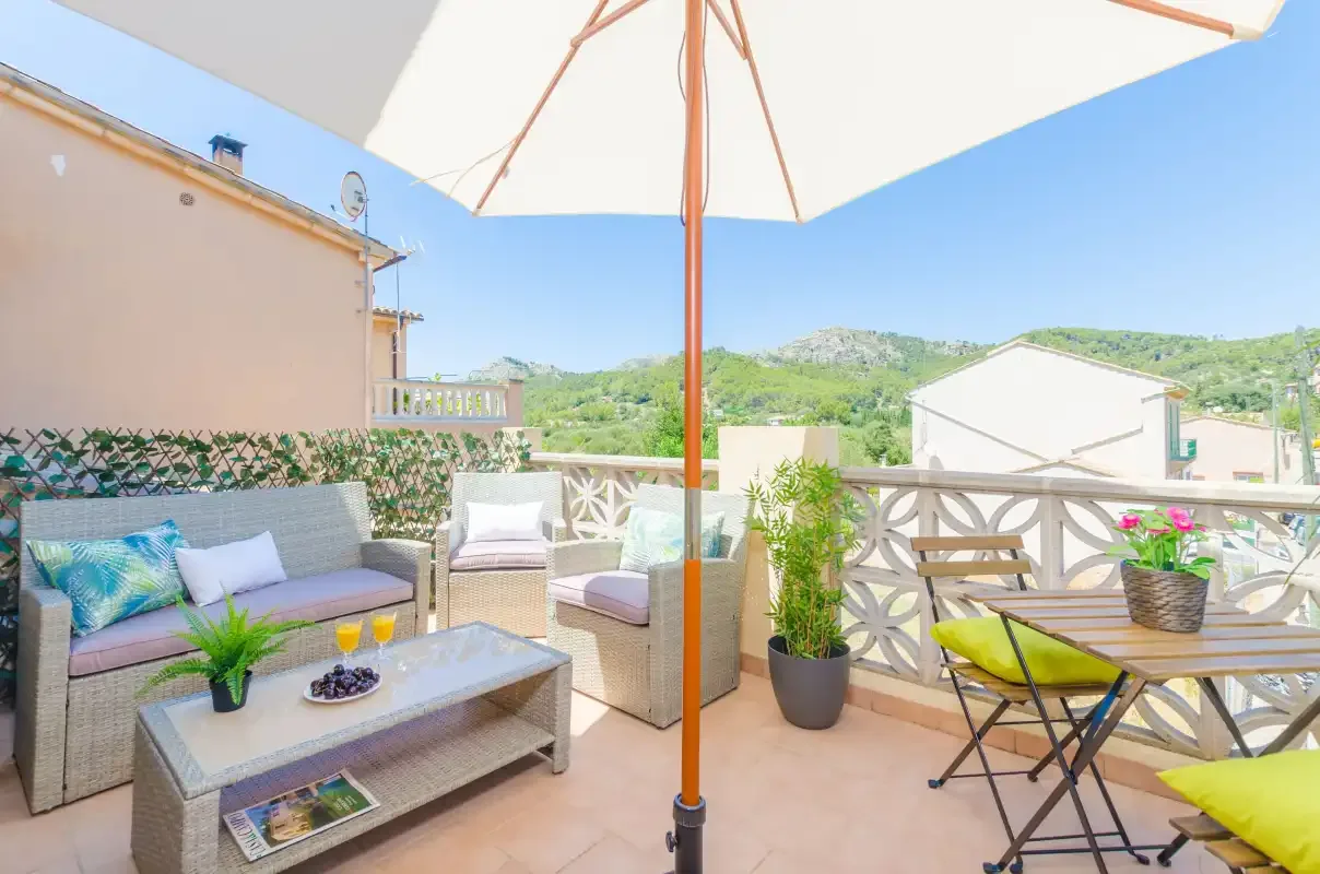 An outdoor terrace with seating, a table, and views of green hills.