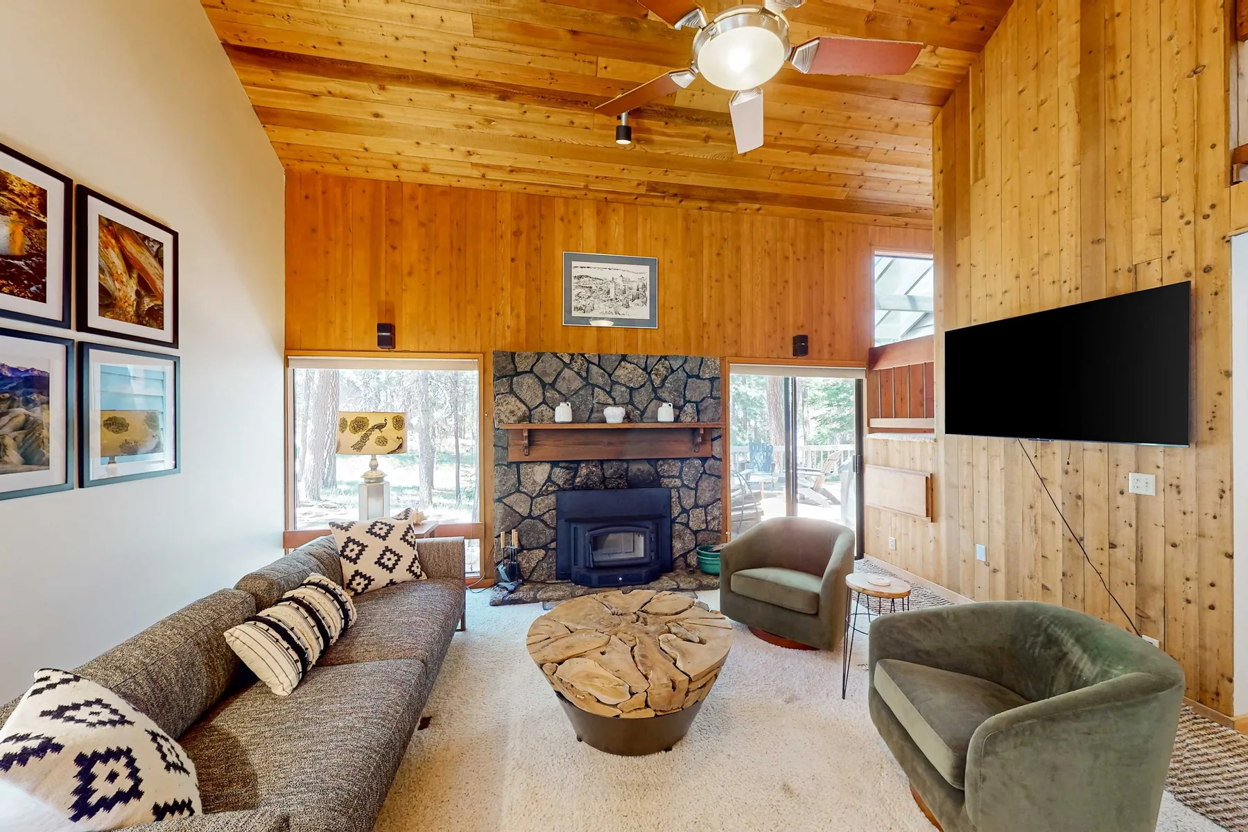 A wood-paneled living room with a stone fireplace, seating, and a wall-mounted television.