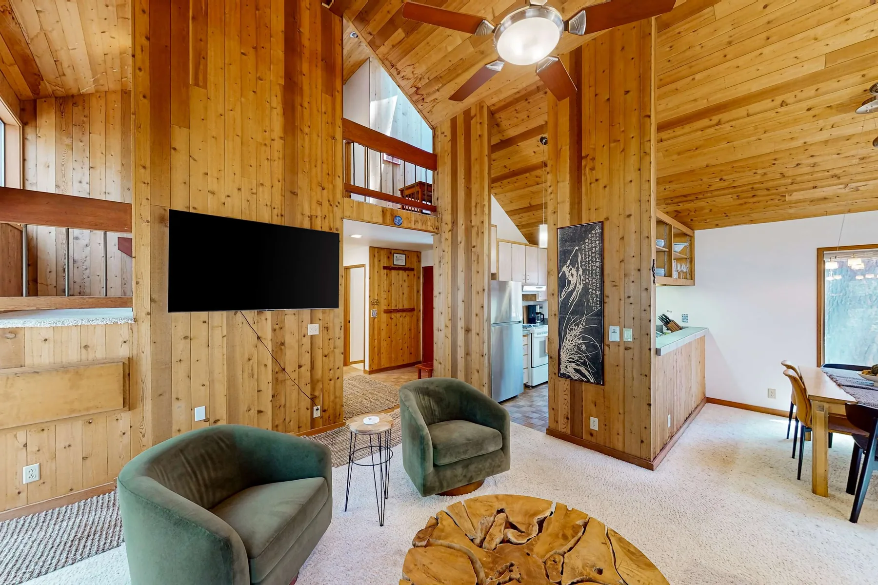 A wood-paneled living area with green seating, a television, and a dining table.