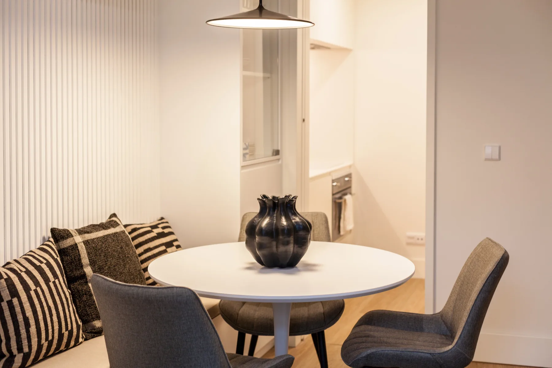 A dining area with a round table, upholstered seating, and a pendant light.
