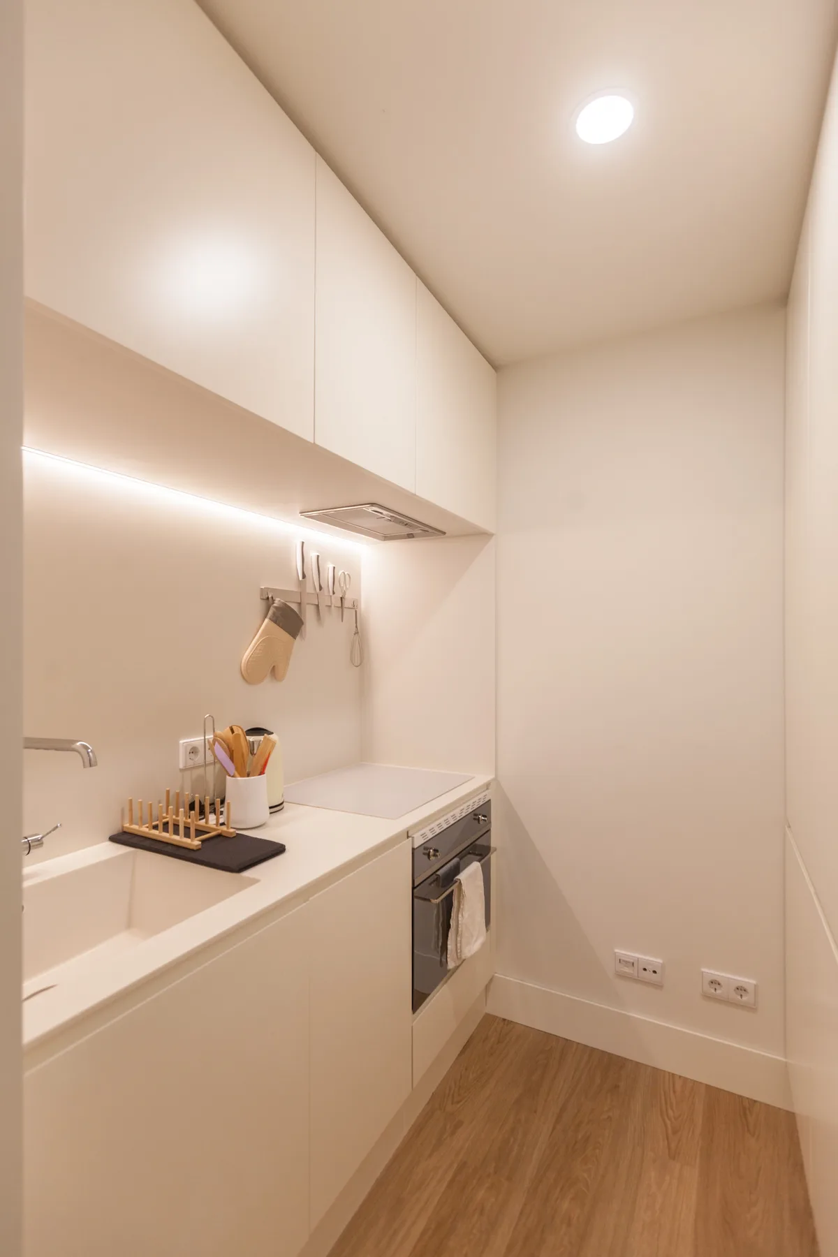A compact modern kitchen with white cabinetry and a built-in oven.