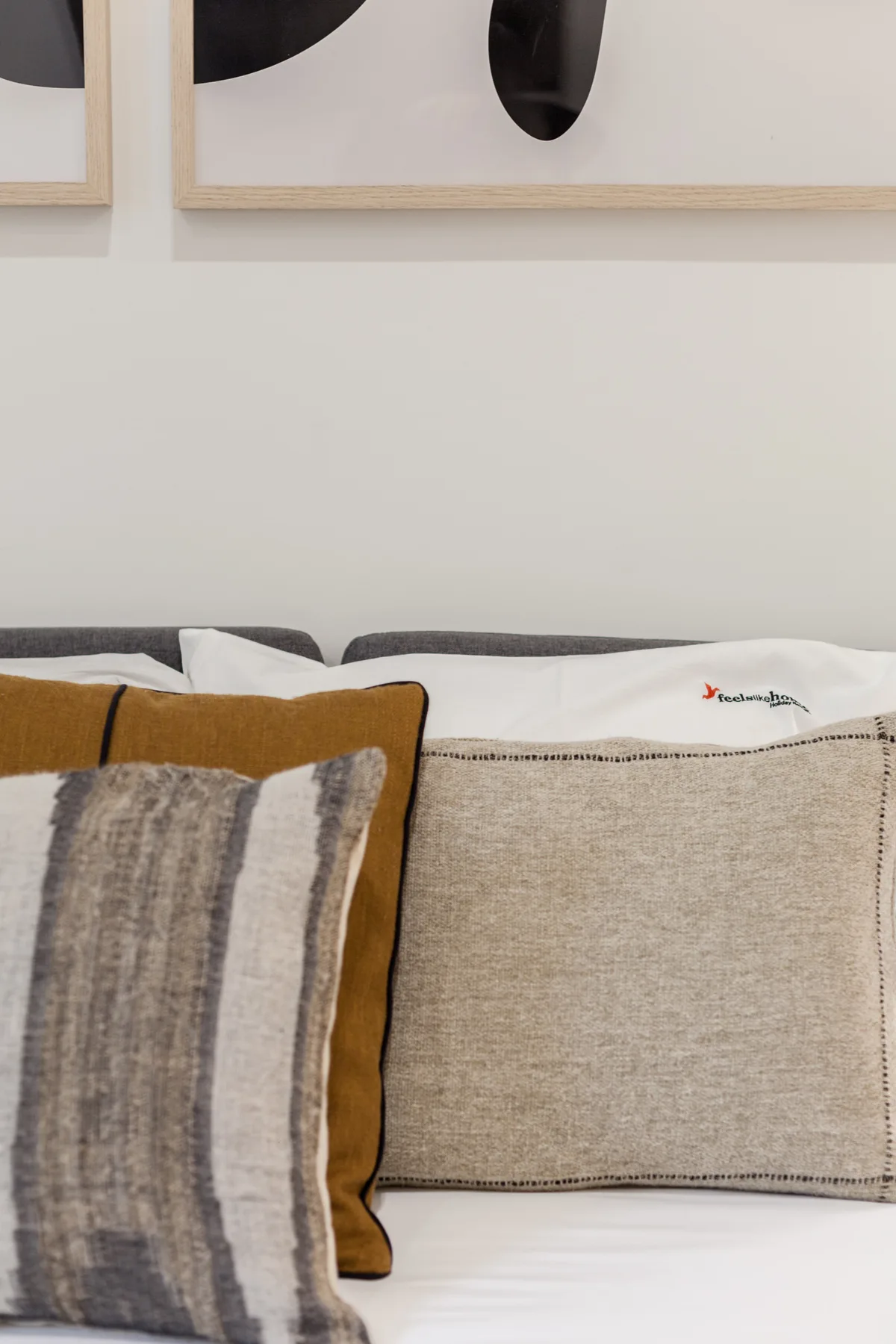A bed with layered decorative pillows sits beneath framed abstract artwork.