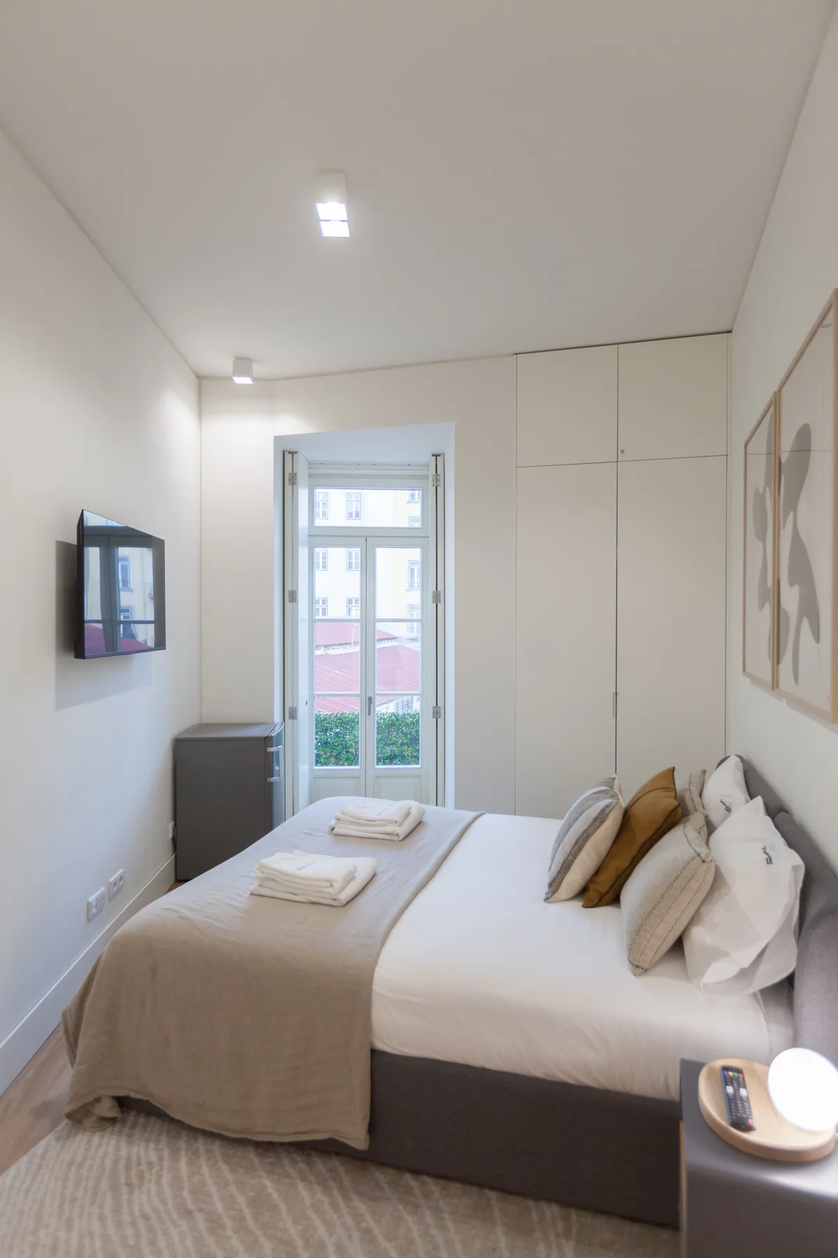 A bright bedroom with a neatly made bed and a window at the far end.