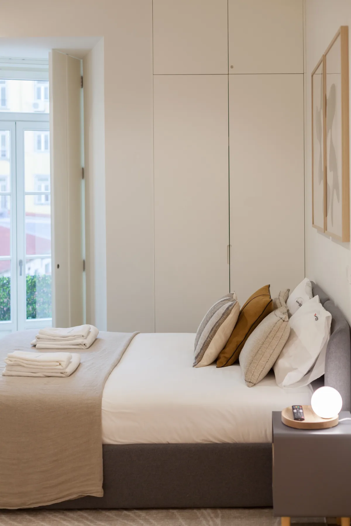 A bedroom with a neatly made bed and folded towels beside a bright window.