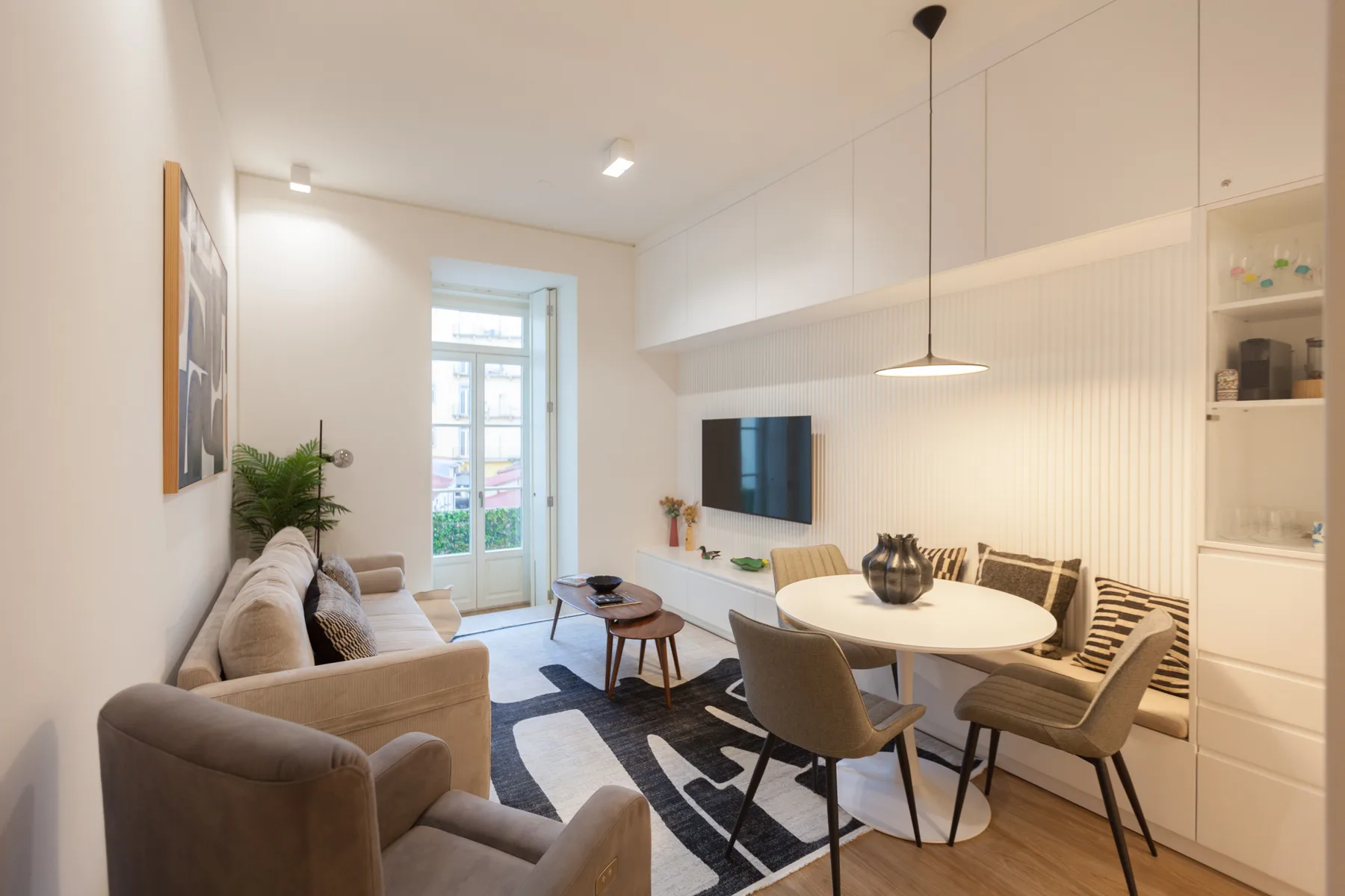 A dining and living area with a round table, seating, and a wall-mounted television.