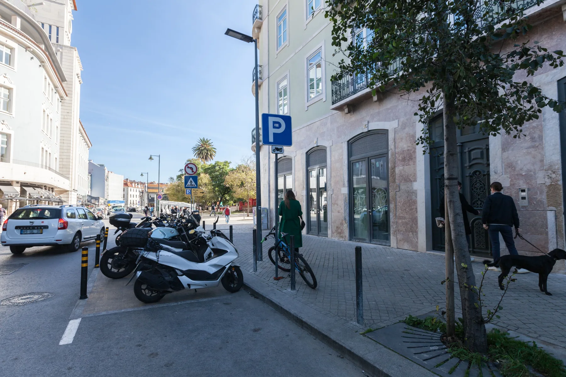 An urban street with parked scooters beside a sidewalk and stone-faced buildings.