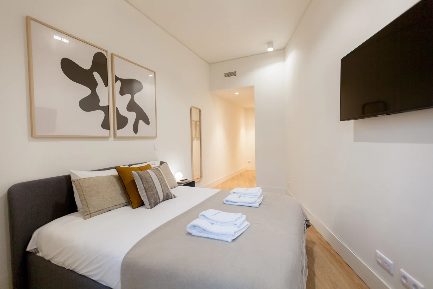 A bedroom with a neatly made bed and abstract artwork above it.