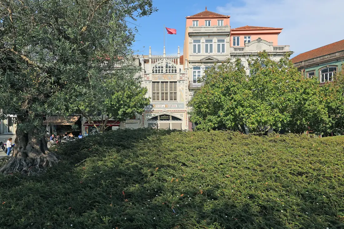 Un jardín urbano con árboles y edificios ornamentados al fondo.