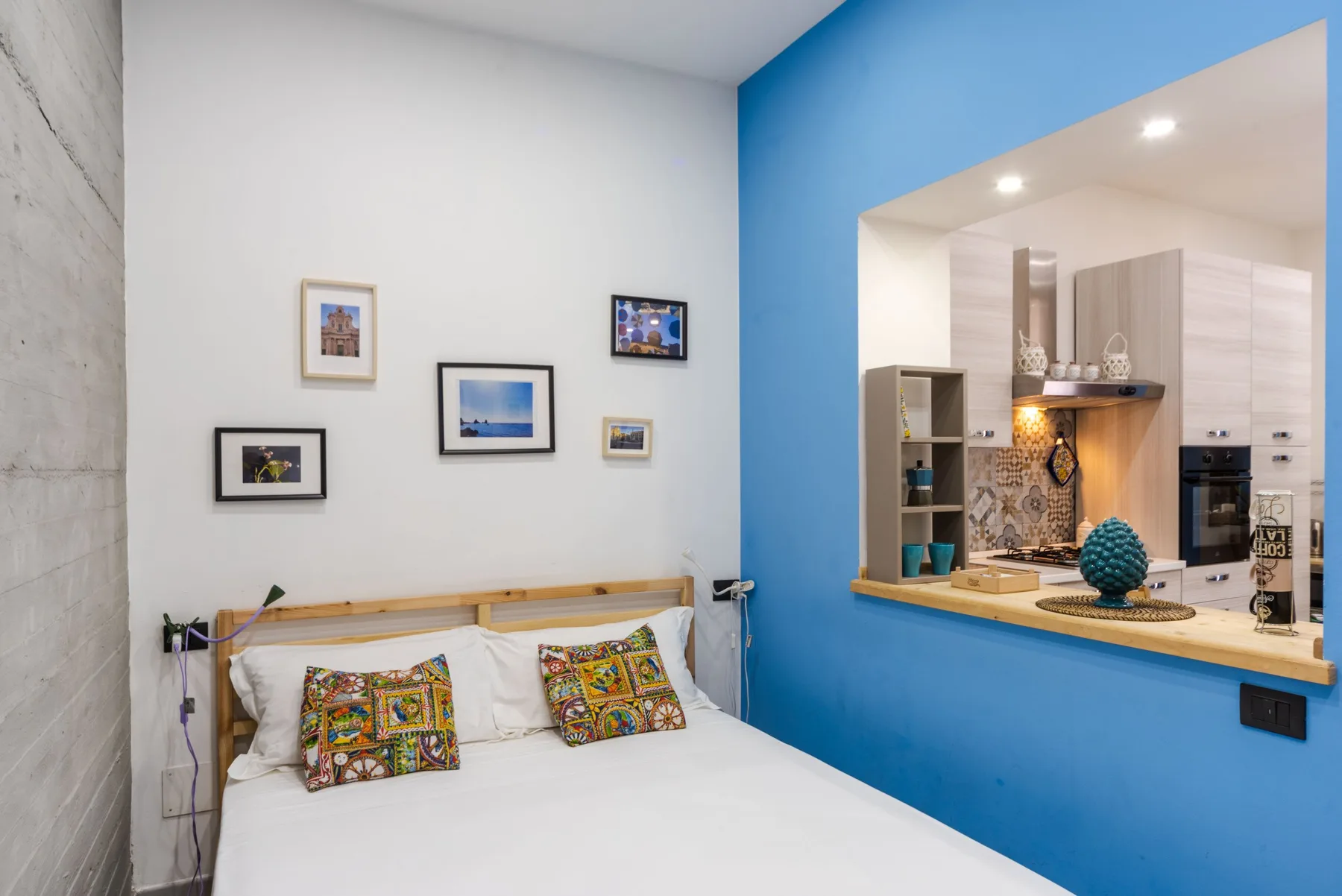 A bedroom with a bed beside a blue wall and a pass-through to the kitchen.