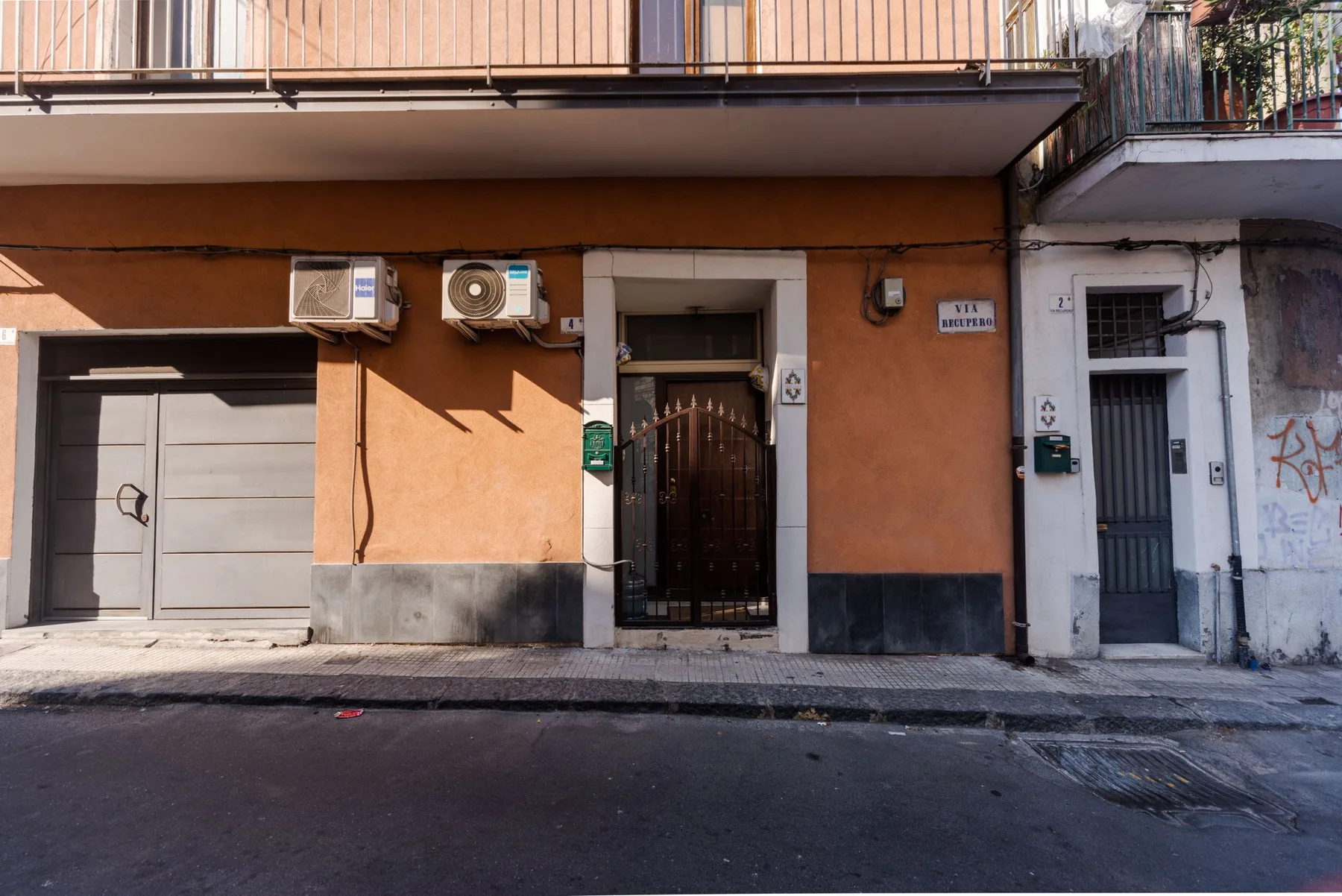 Street-level view of an orange building facade with a gated entrance and garage door.