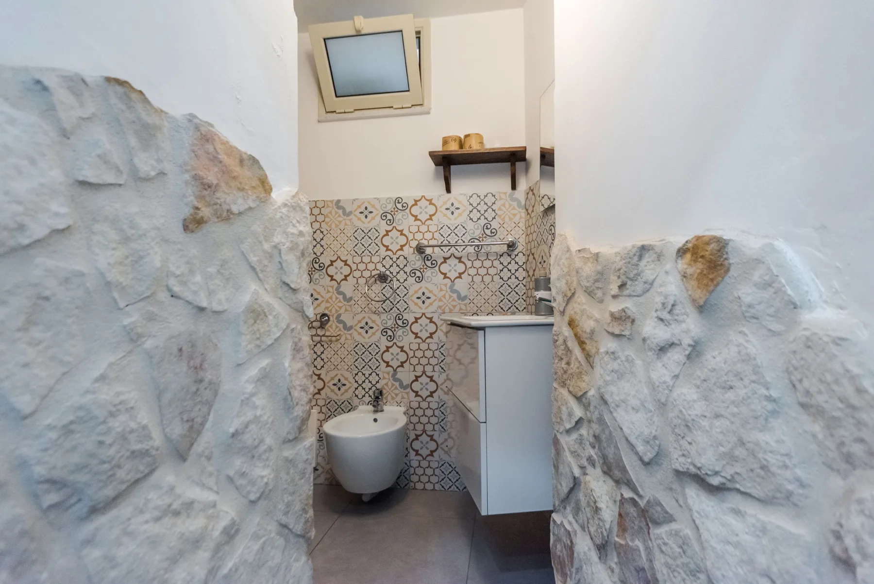 A compact bathroom with a toilet, sink, and patterned tile wall.