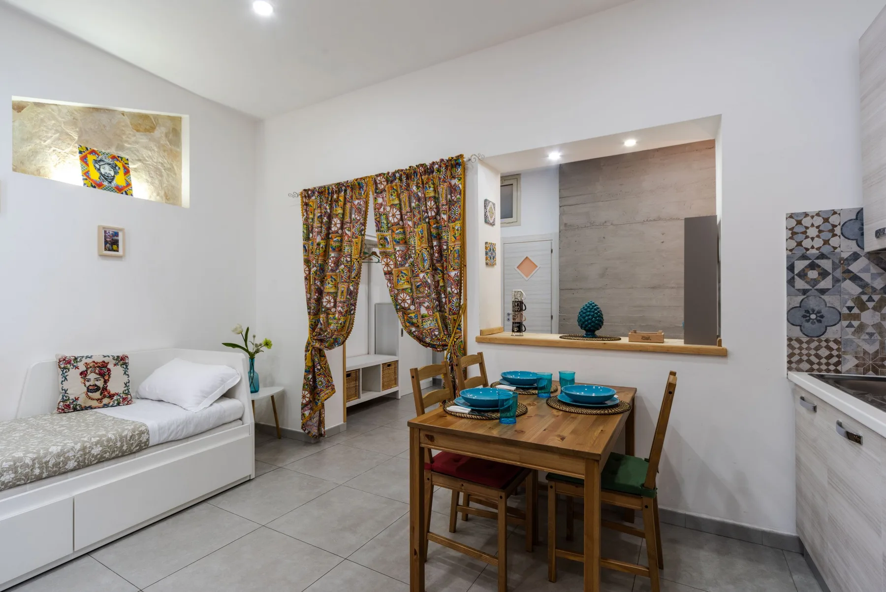 A dining area with a wooden table and chairs beside a small bed.