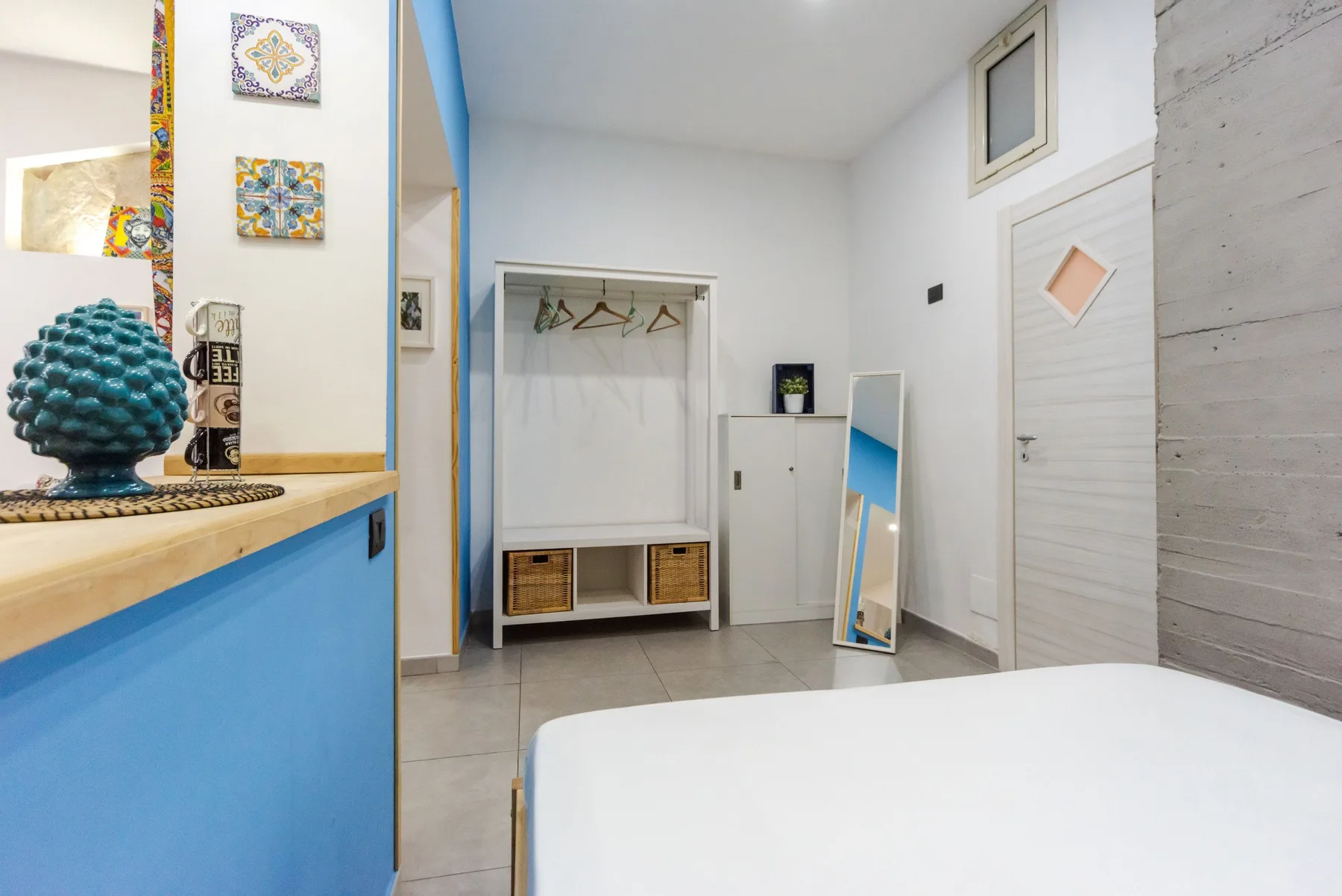 A bright bedroom with a white bed, a wardrobe, and a full-length mirror.