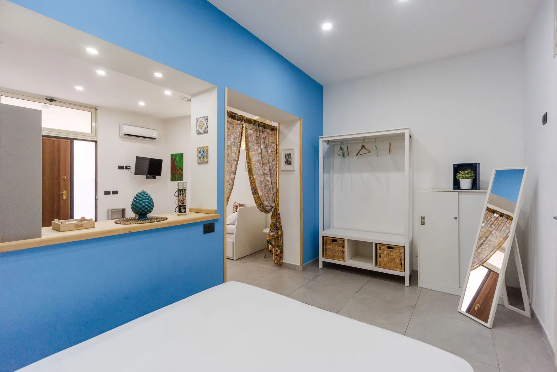 A bright bedroom with a blue wall, a curtained doorway, and an open clothes rack.