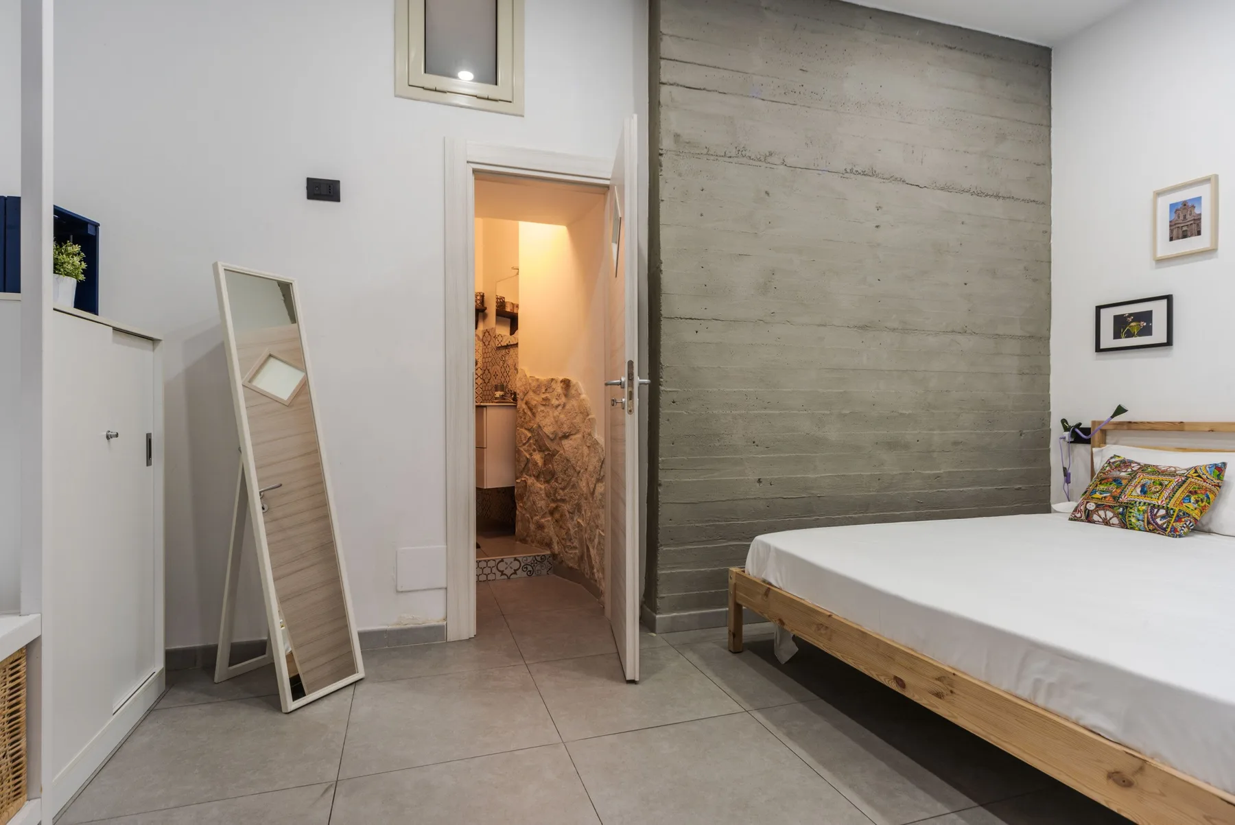 A bedroom with a bed beside a textured gray wall and an open doorway.