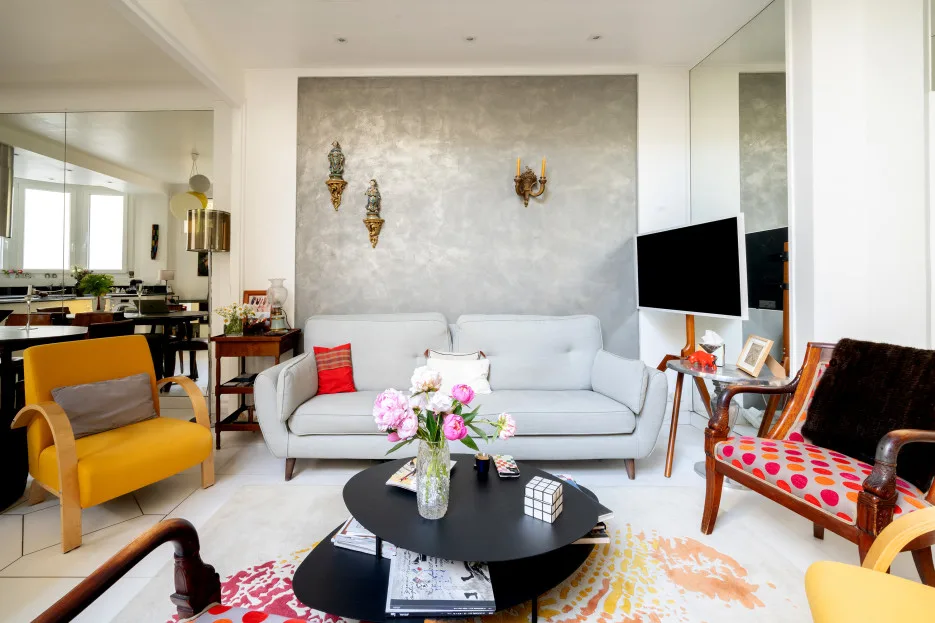 A bright living room with a white sofa, a black coffee table, and colorful seating.
