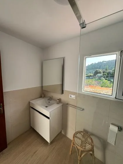A bathroom with a sink vanity, mirror, and window overlooking greenery.