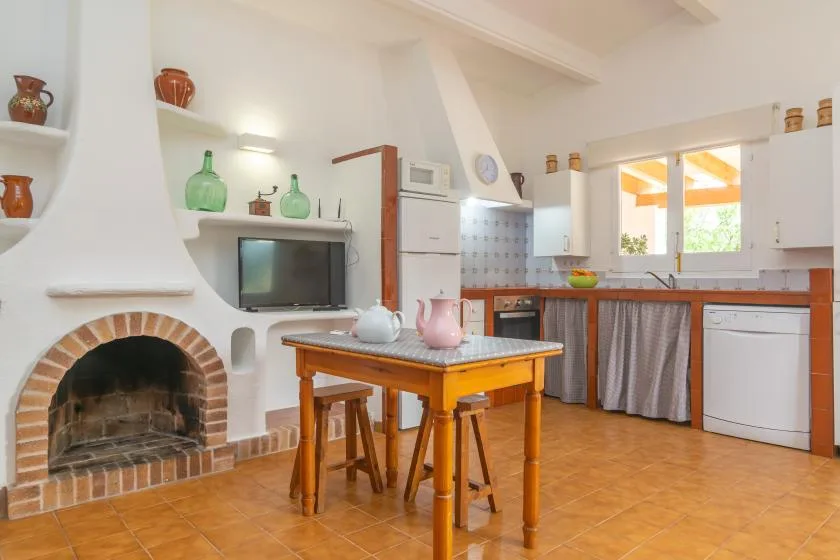 A bright kitchen with a tiled table, fireplace, and cabinets.